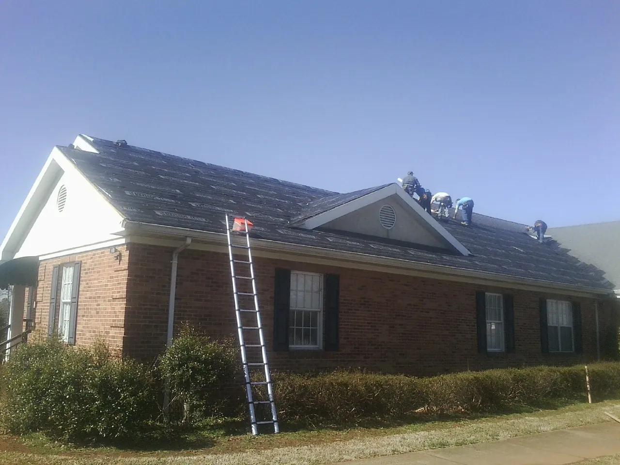 Crew tearing shingles off a brick ranch roof with a ladder set — Emergency Roof Repair work by our crew in Indianapolis