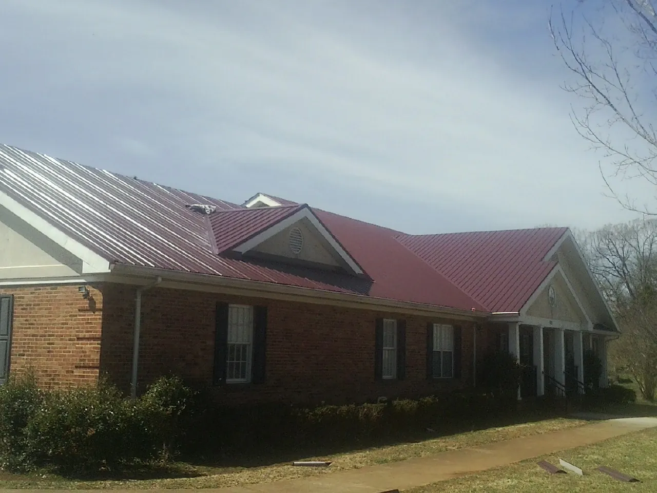 Red metal roof with gabled entries on a long brick building, from a Hail Damage Roof Repair job in Indianapolis