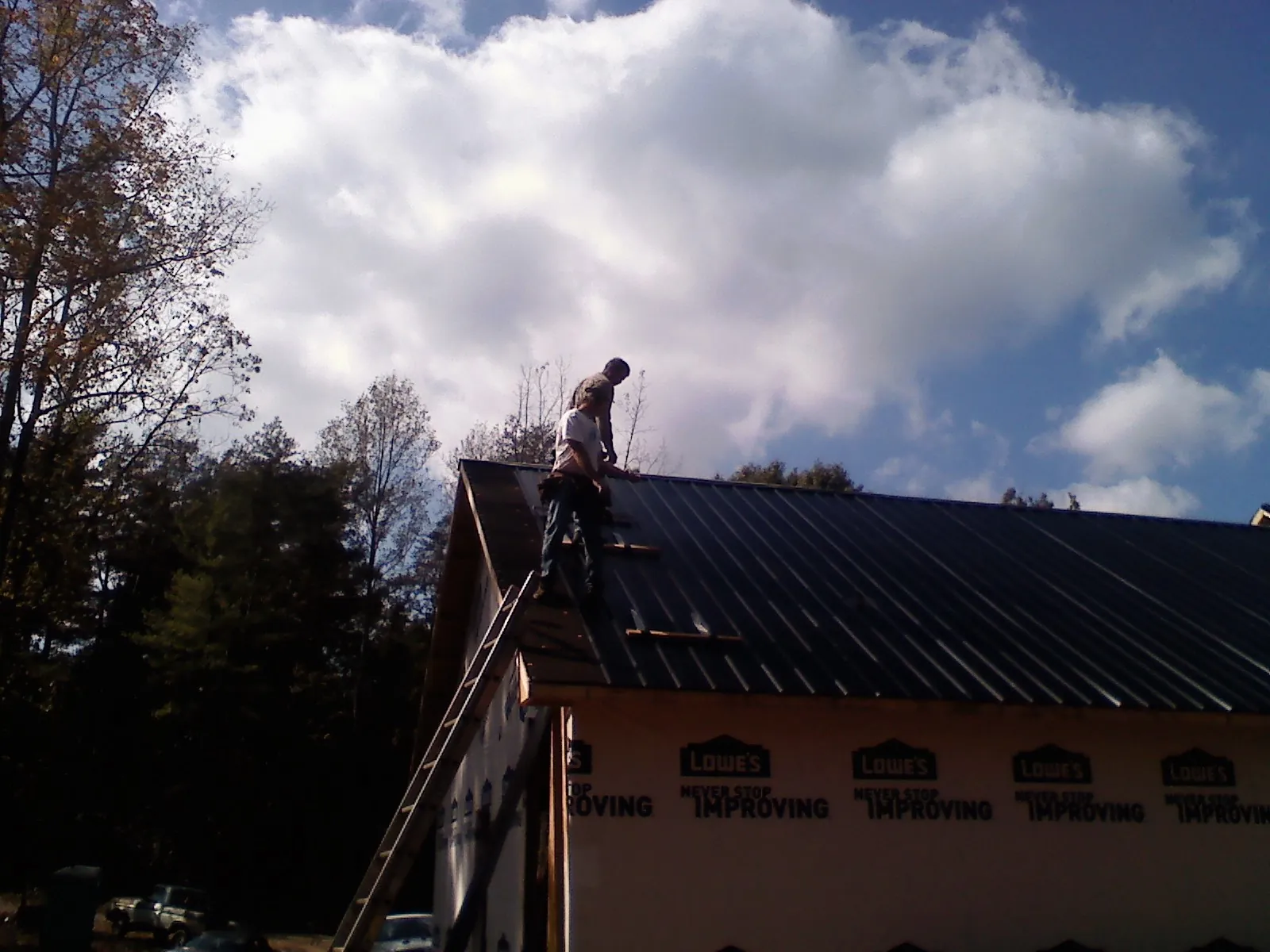 Roofer fastening dark metal panels high against a cloudy sky, from a Roof Inspection job in Indianapolis