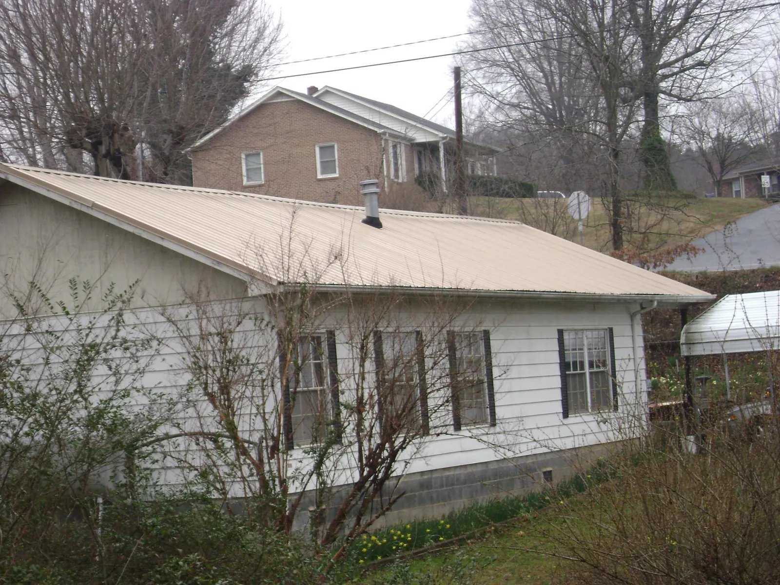 Tan metal roof on a white sided house set into a hillside — Commercial Roofing by Roofing Brothers in Indianapolis