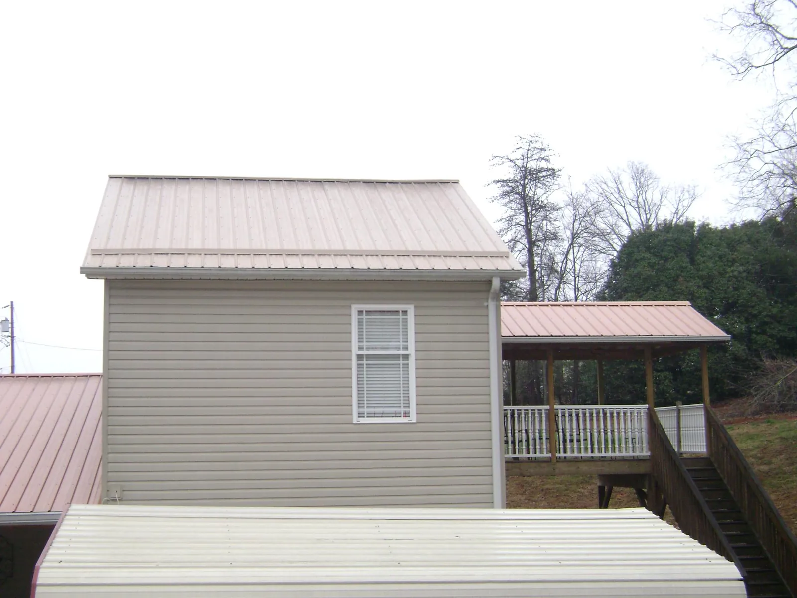 Tan metal roofs on a two story addition and attached porch, from a Roof Replacement job in Indianapolis